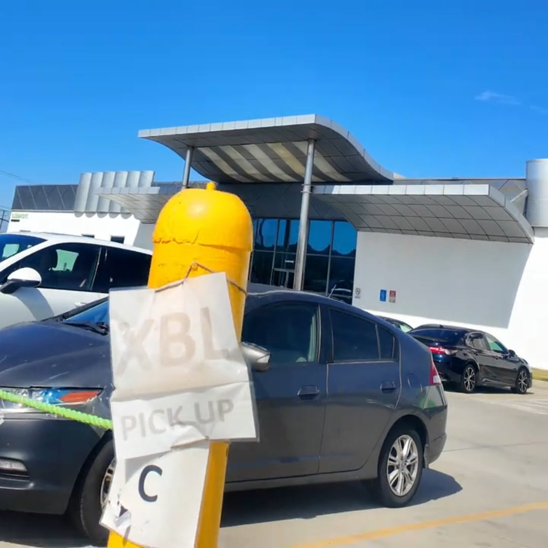 Car parked in a parking lot with a yellow and white 'XBL Pickup' sign in the foreground.
