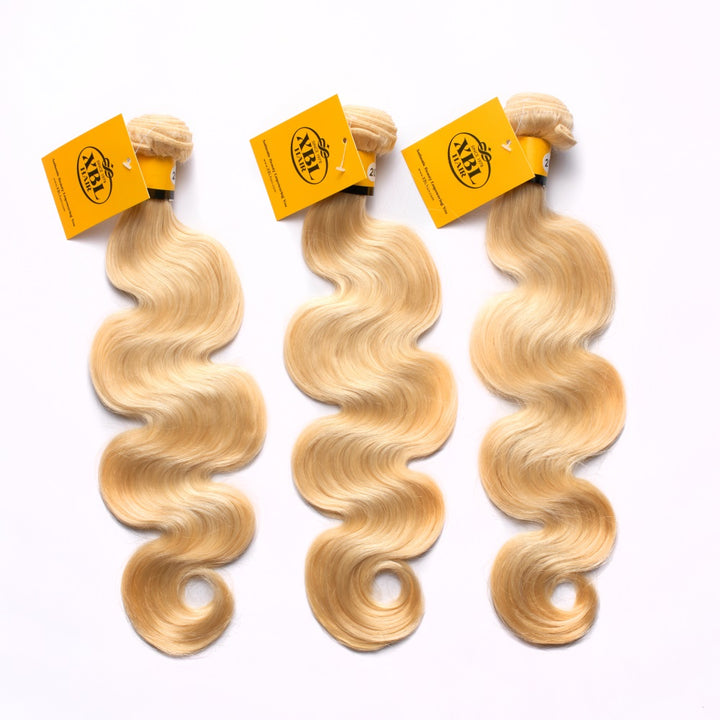 Three bundles of 613 blonde body wave hair extensions laid out with hair volume and tags visible.