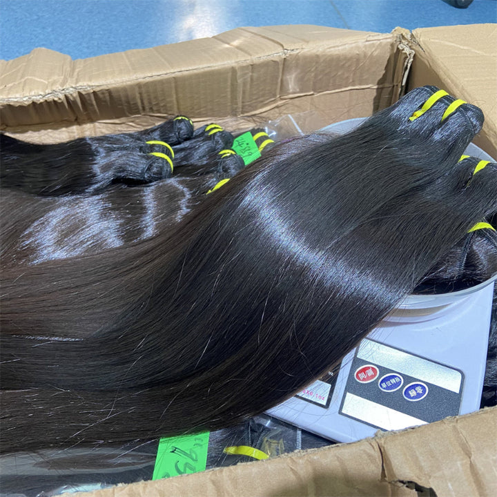 Three bundles of straight raw human hair with hair extensions visible, placed in a carton with a digital scale for measurement.