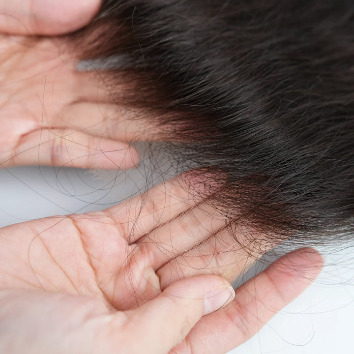 Close-up of a hand holding a clump of black hair against a light background