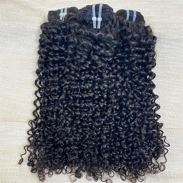 Three bundles of curly black hair weaves placed on a textured beige surface.